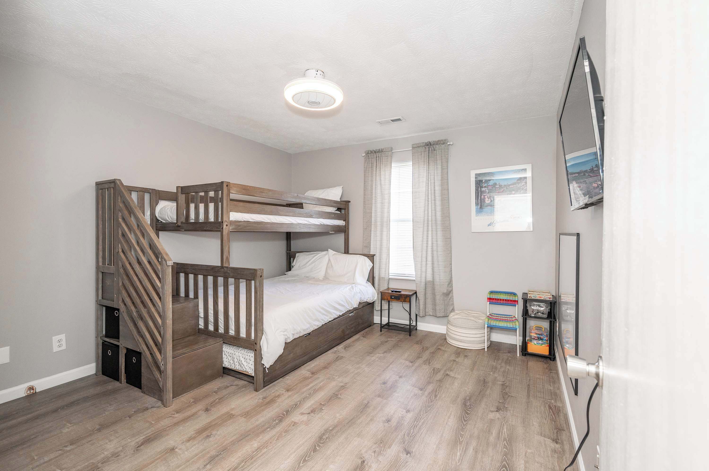 A bedroom with a bunk bed, a small bedside table, a mirror, and a TV mounted on the wall.