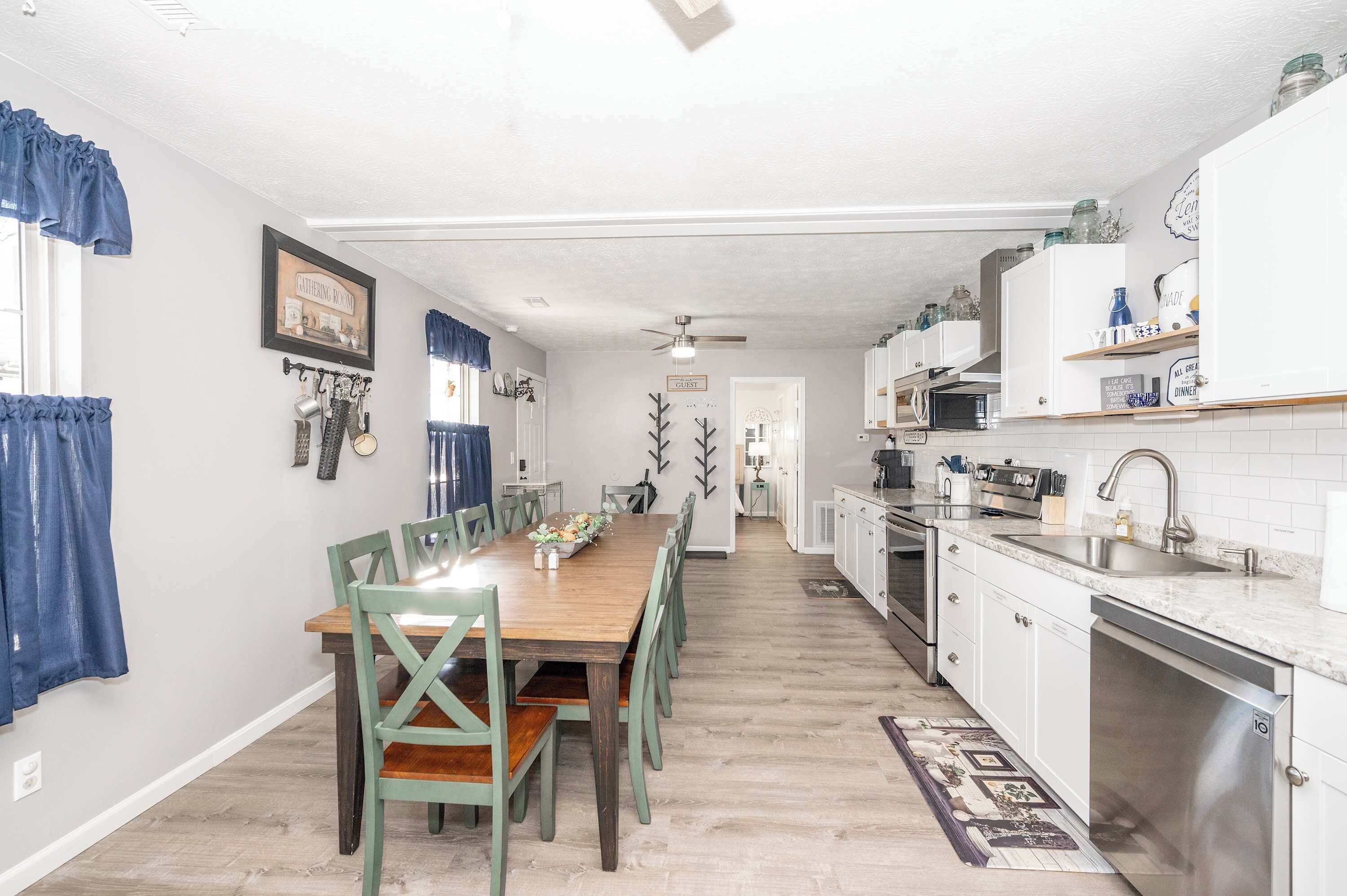 Une cuisine avec des meubles blancs, une table à manger en bois et un ventilateur de plafond.