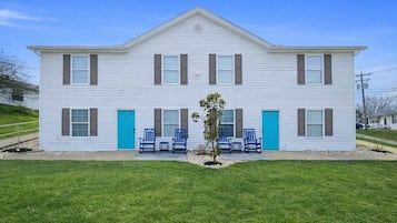 A two-story building with a symmetrical facade, a central entrance, and a small tree in the front yard.