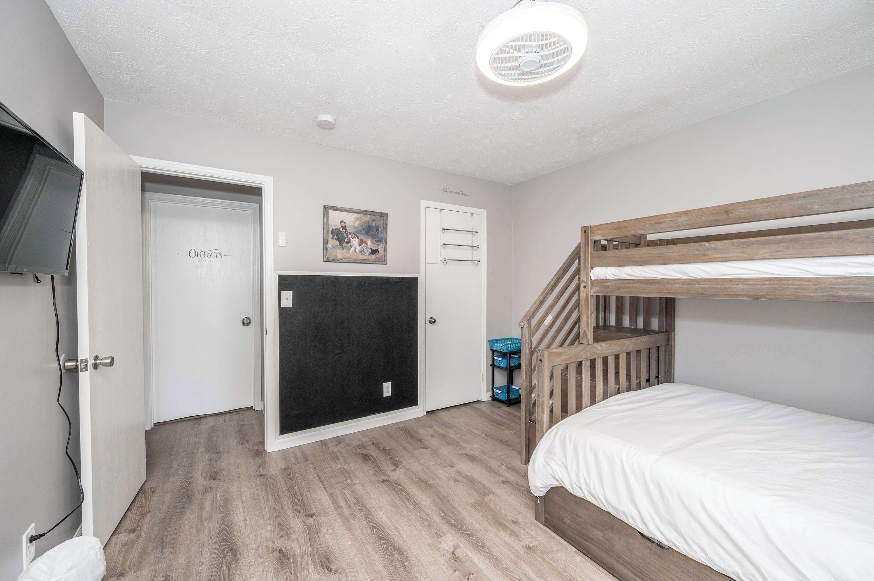Une chambre avec un lit superposé, une porte avec une pancarte, un tableau accroché au mur et un luminaire au plafond.
