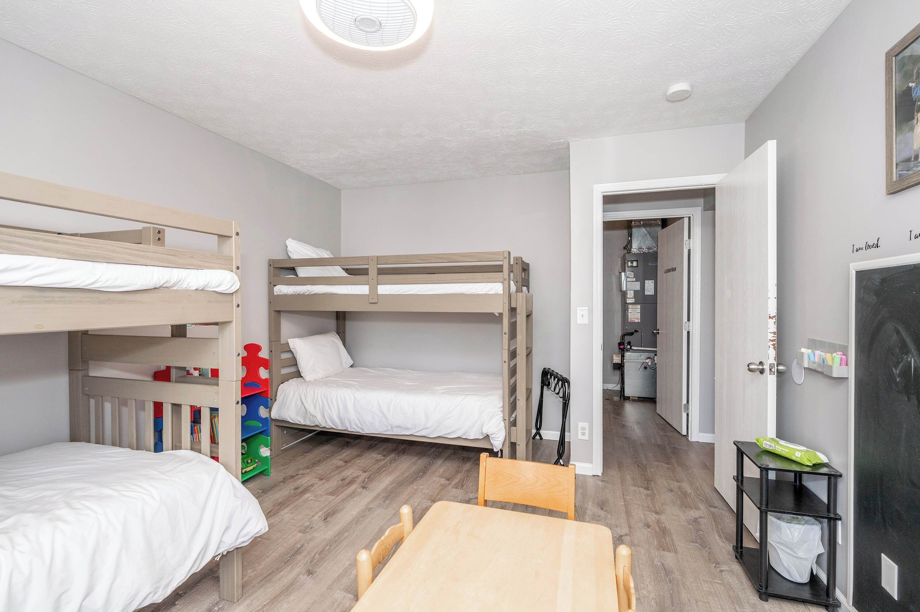 Une pièce avec des lits superposés, une table en bois et une porte donnant sur un couloir.
