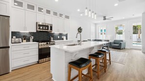 A modern kitchen with white cabinetry, stainless steel appliances, and a large island with bar stools.