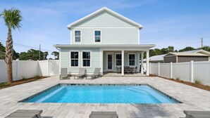 A two-story house with a swimming pool, white exterior, and a covered patio with outdoor furniture.