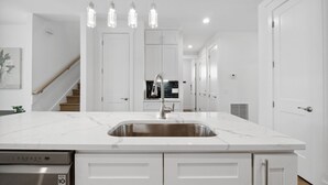 A modern kitchen with white cabinetry, a stainless steel sink, and pendant lighting.