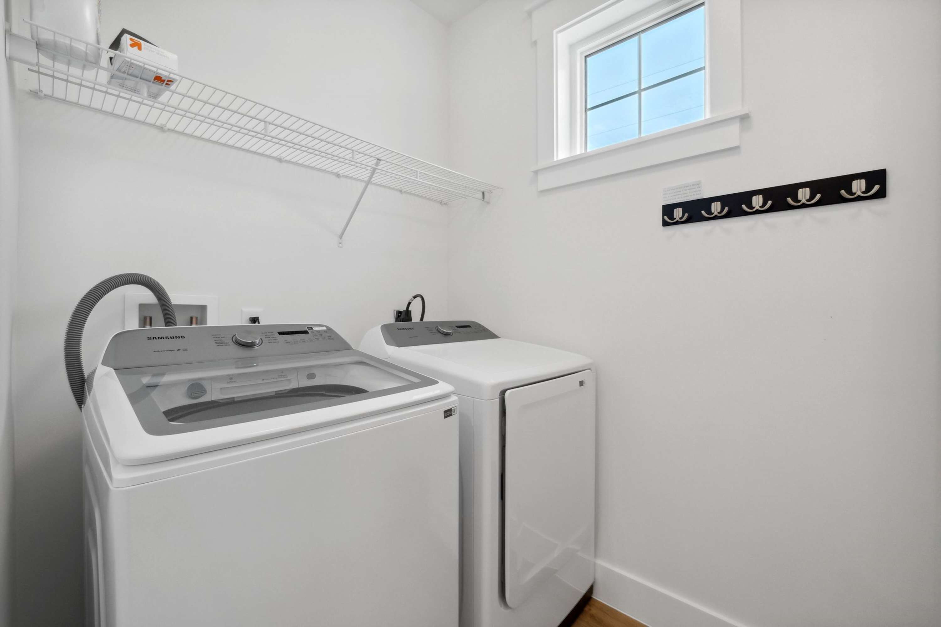A laundry area with a Samsung washer and dryer, a drying rack, and a window.