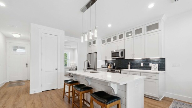 A modern kitchen with white cabinets, a black backsplash, and a central island with stools.