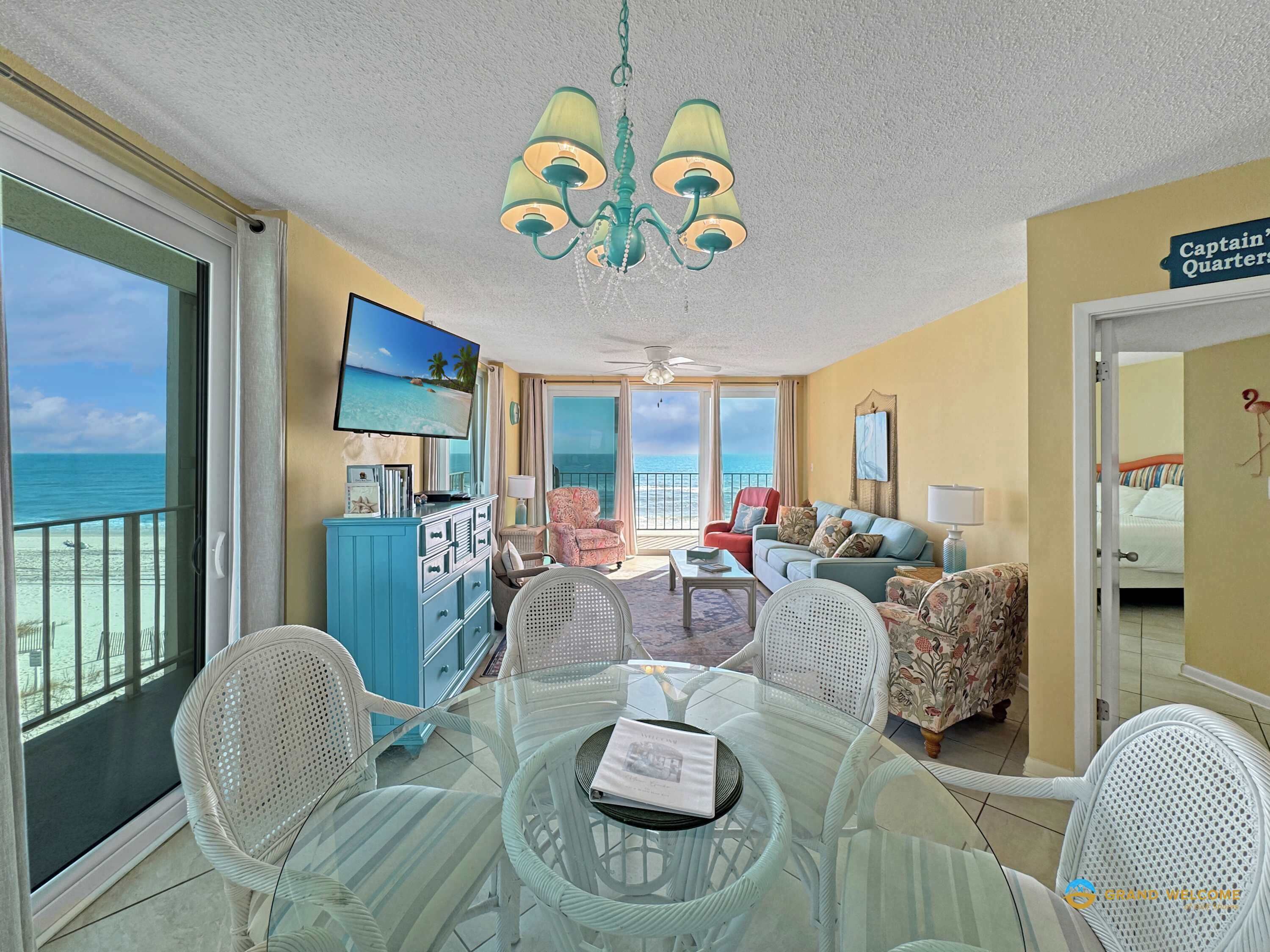 A spacious balcony with a clear view of the ocean, a dining area with a glass table and chairs, and a living room with a television and comfortable seating.