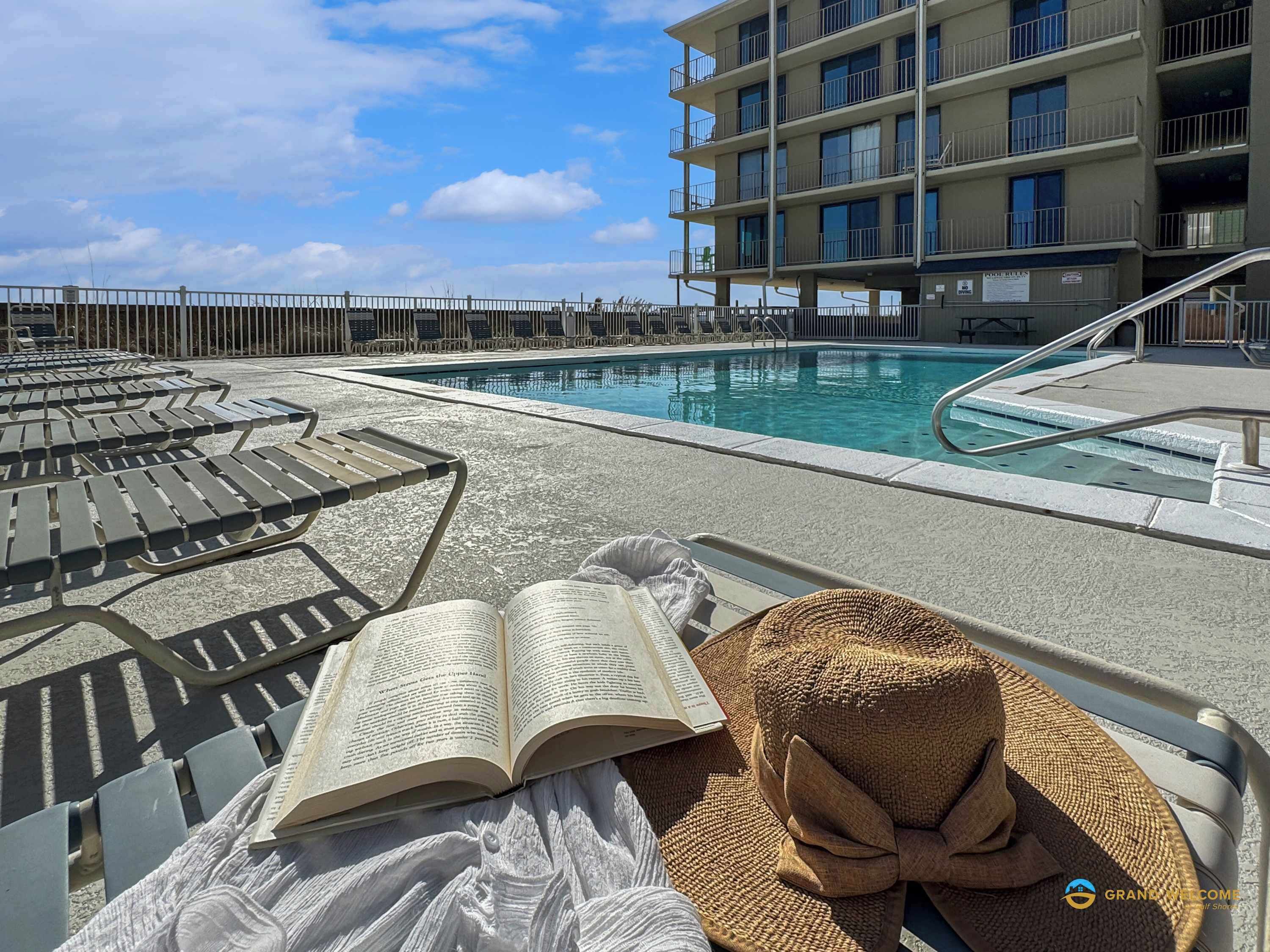 A poolside area with lounge chairs, a pool, and a building in the background.