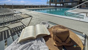 A poolside area with lounge chairs, a pool, and a building in the background. - Oceanfront Oasis Beachfront Condo w/ Views! (Gulf Shores)