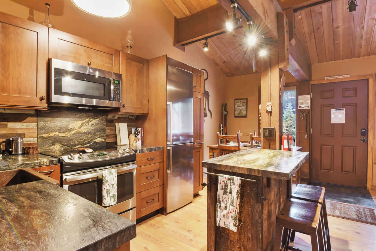 A kitchen with wooden cabinets, a stainless steel microwave, a refrigerator, and a marble countertop.