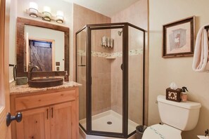 Un baño con tocador de madera, cabina de ducha de vidrio y un inodoro con una caja decorativa.