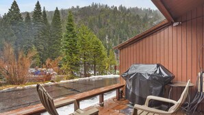 Une terrasse en bois avec deux chaises et un barbecue couvert, offrant une vue sur un paysage enneigé et des collines boisées.