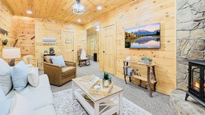 A cozy log cabin interior with a fireplace, a mounted TV, and a stone wall.