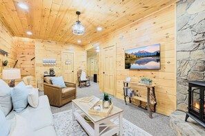 A cozy log cabin interior with a fireplace, a mounted TV, and a stone wall. - Misty Creek Cabin Private 3 BDR w/ Game Room! (Blue Ridge)