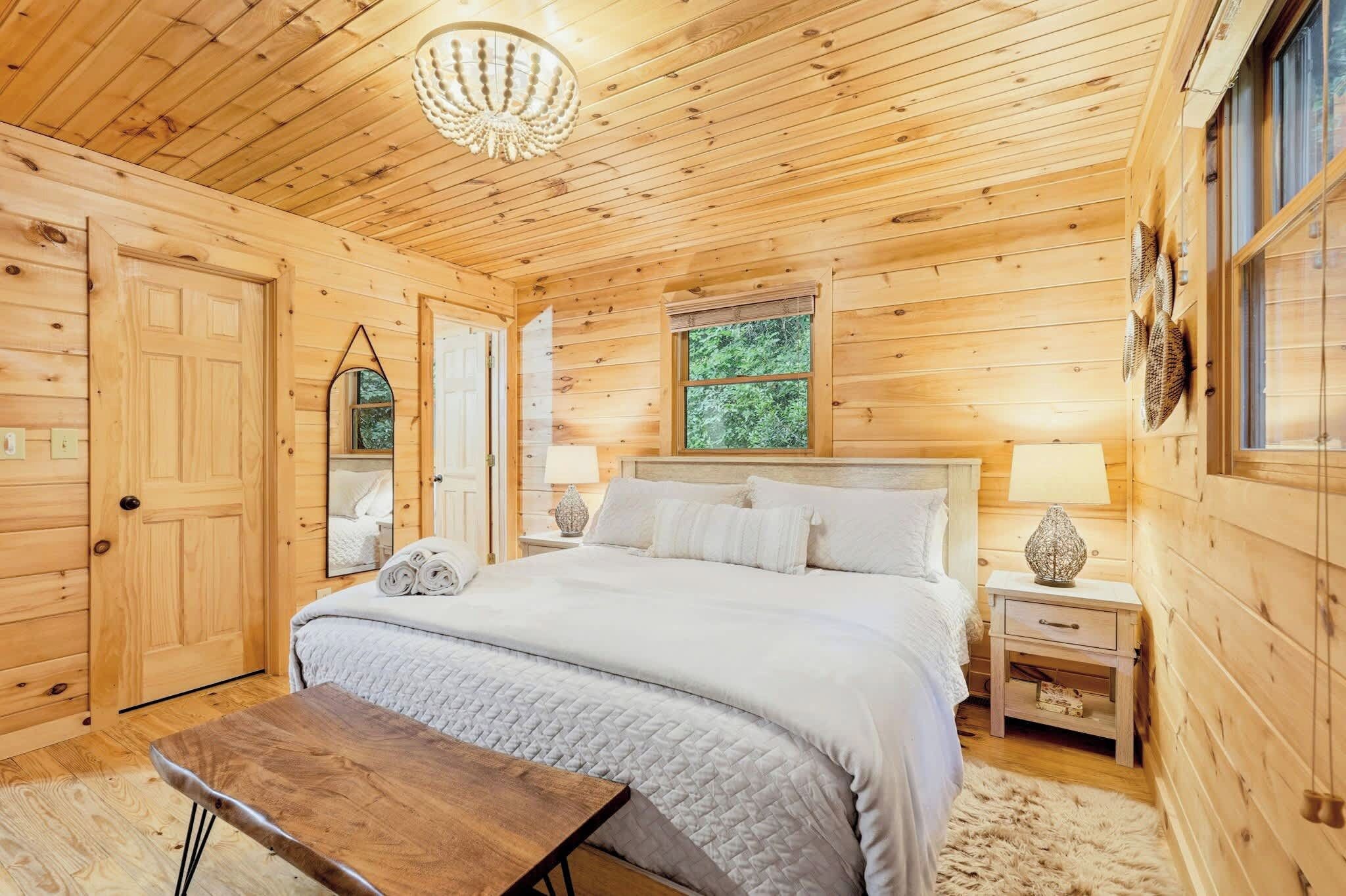 A wooden cabin bedroom with a bed, bedside tables, a mirror, and a chandelier.