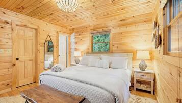 Un dormitorio de cabaña de madera con una cama, mesitas de noche, un espejo y una araña.
