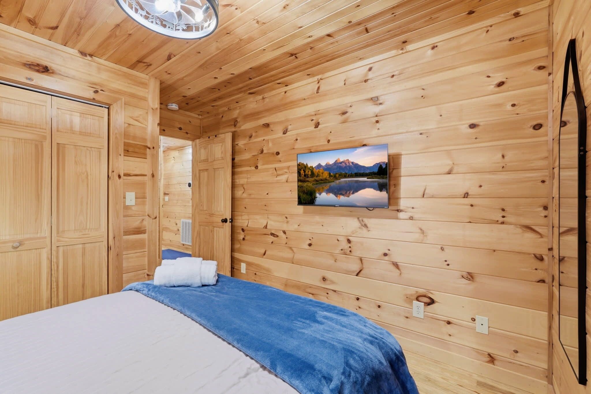 A wooden-paneled room with a bed, a wall-mounted TV, and a door.