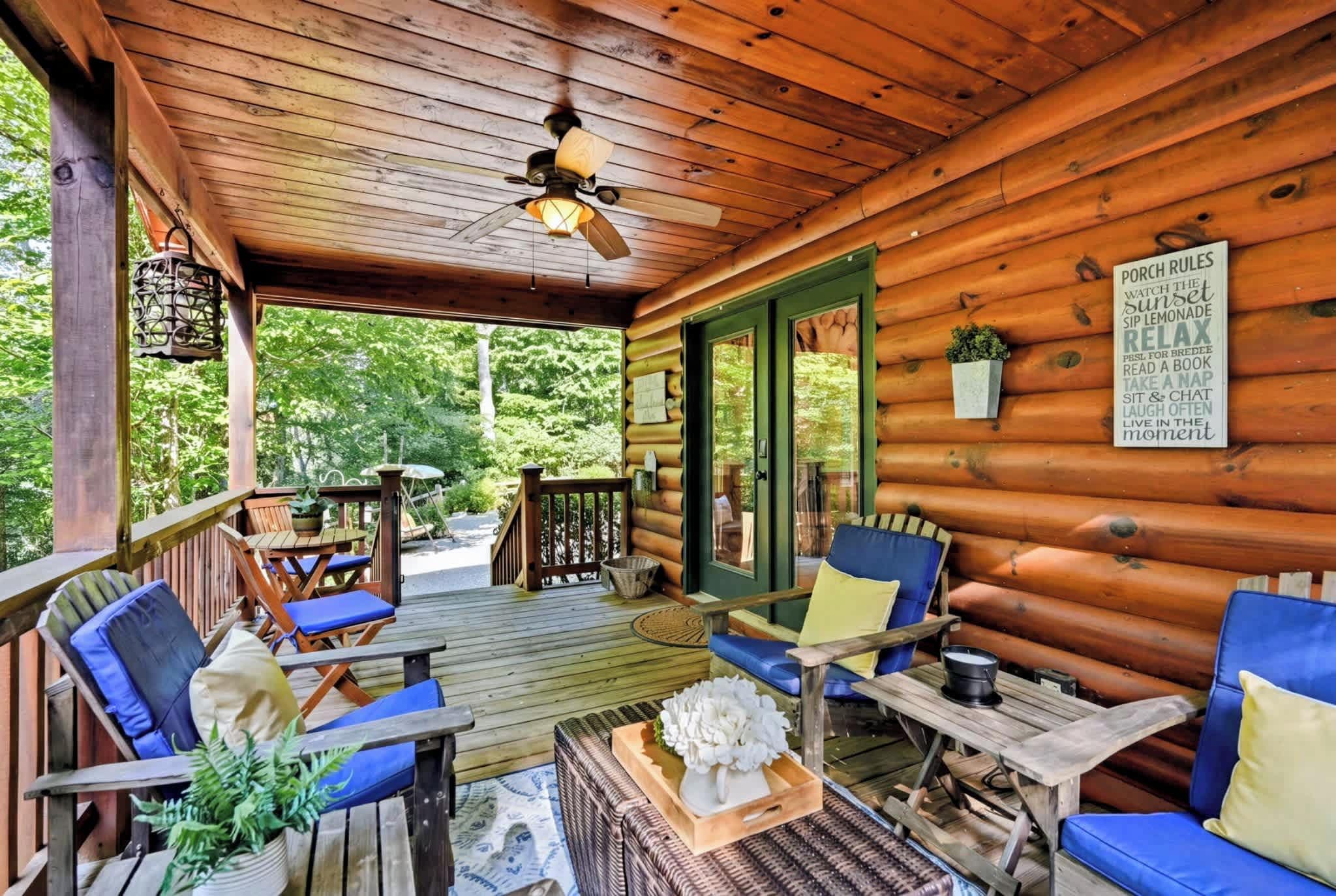 A wooden cabin with a porch area featuring outdoor seating, a ceiling fan, and a sign with relaxation tips.