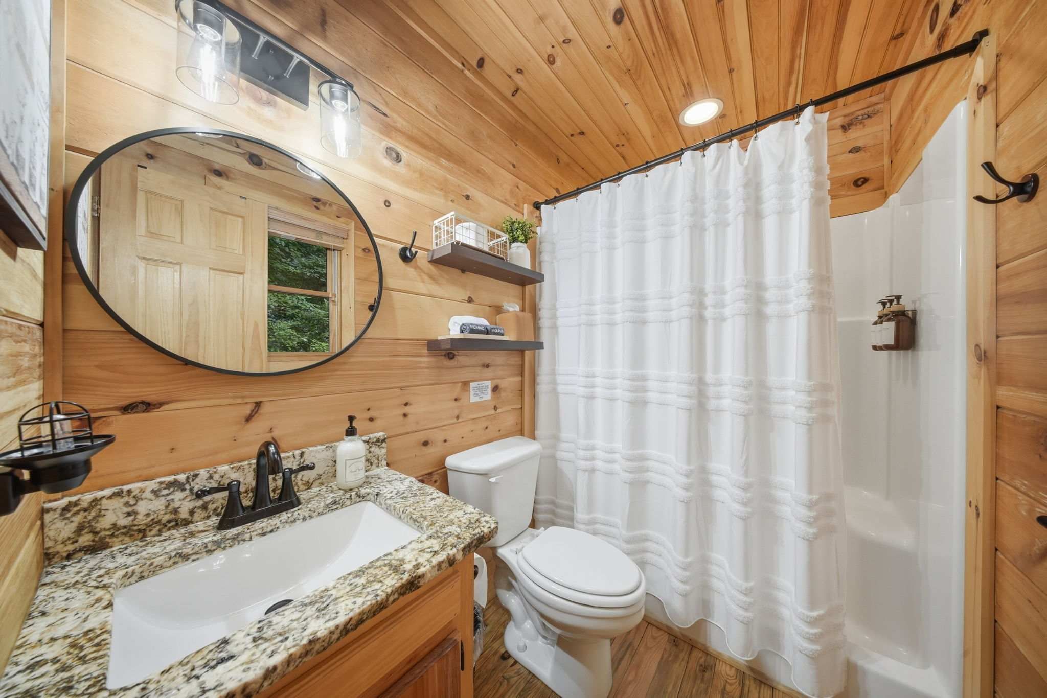 A wooden cabin bathroom with a granite countertop sink, a toilet, a shower curtain, and a mirror.