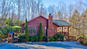 A log cabin with a chimney, a porch, and a covered outdoor seating area.