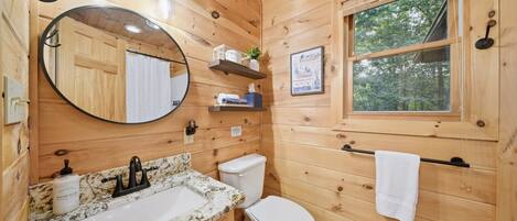 Baño de cabaña de madera con lavamanos, inodoro, espejo y ventana.