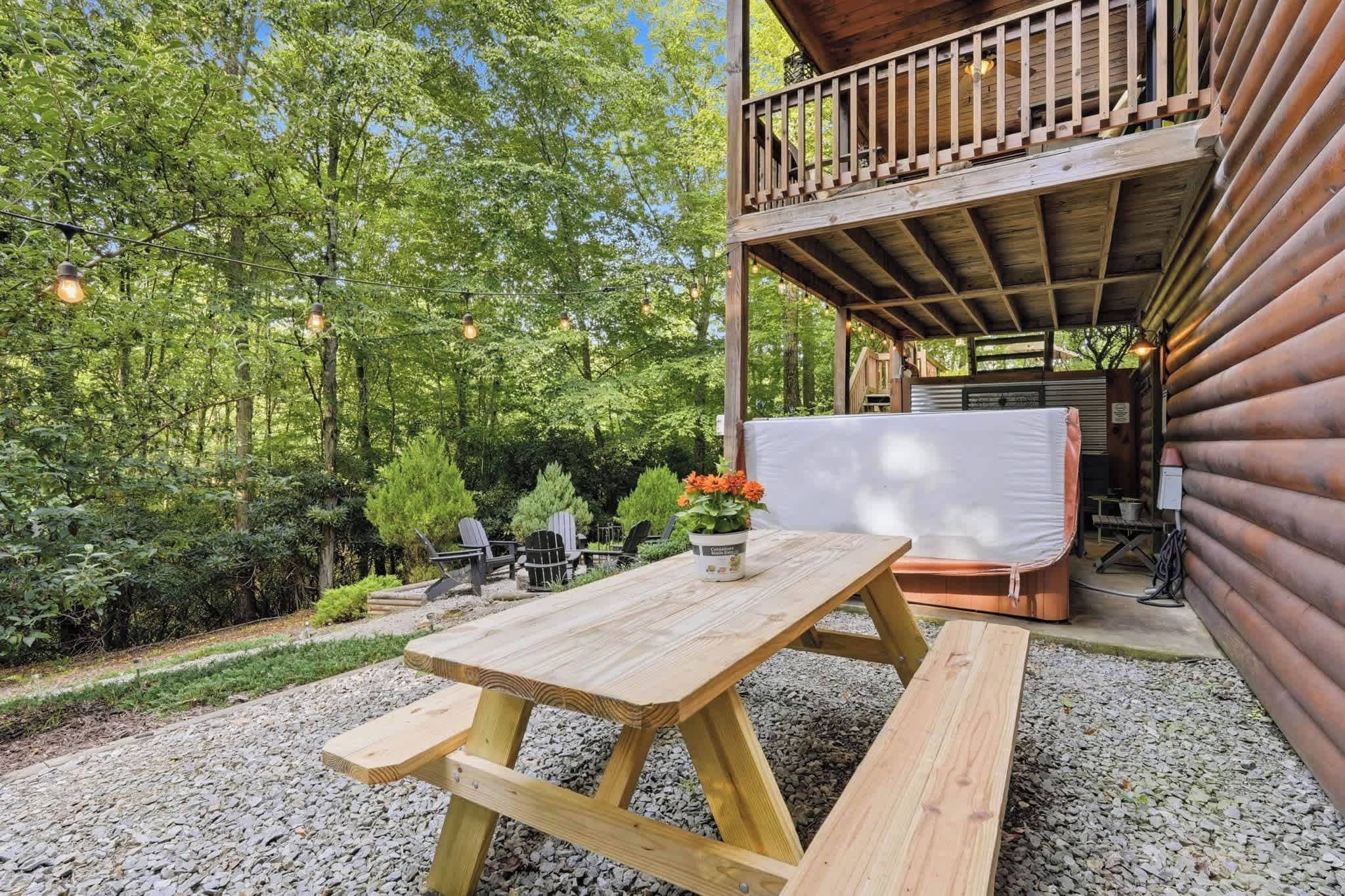 A wooden deck with a picnic table and benches, surrounded by trees and a covered seating area.