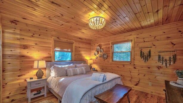 A wooden cabin bedroom with a bed, nightstands, a chandelier, and wall decorations.
