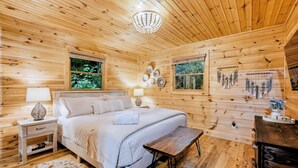 A wooden cabin bedroom with a bed, bedside tables, and a chandelier. - Misty Creek Cabin Private 3 BDR w/ Game Room! (Blue Ridge)
