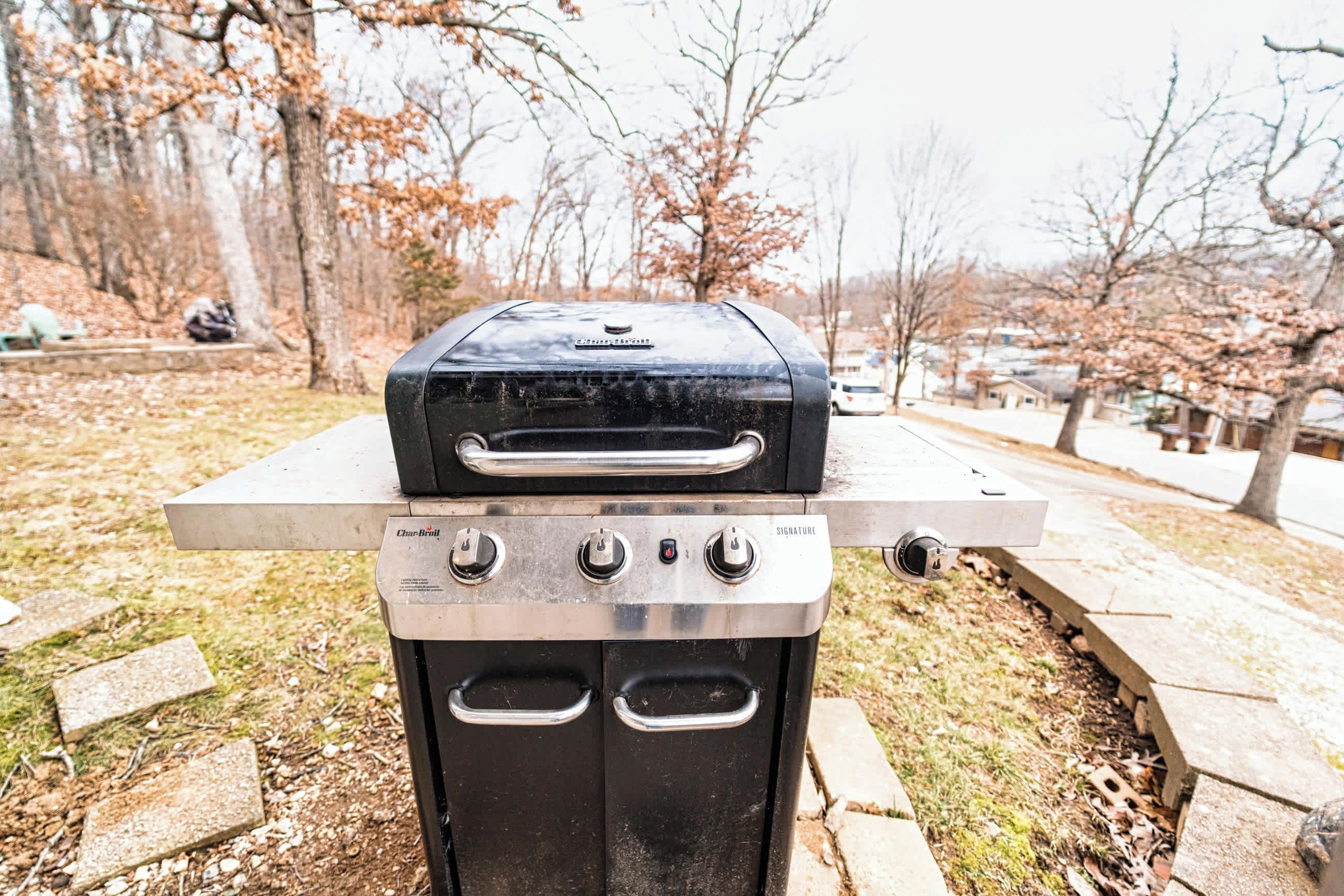 A portable grill with a digital display and control knobs, placed on a concrete surface outdoors.