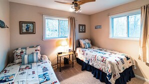 Un dormitorio con dos camas, un ventilador de techo y dos ventanas con cortinas.