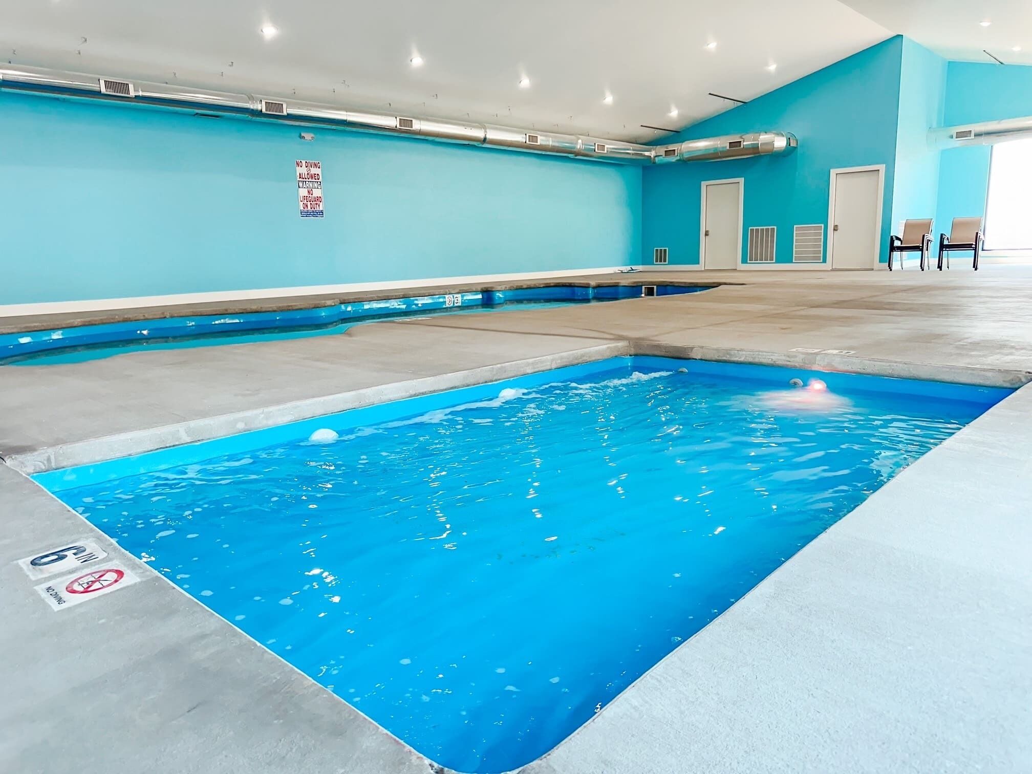 Ein Hallenbad mit einem Schild 'Tauchen verboten', einem Hinweisschild für einen Rettungsschwimmer und einer Tiefenmarkierung von 6 Metern.