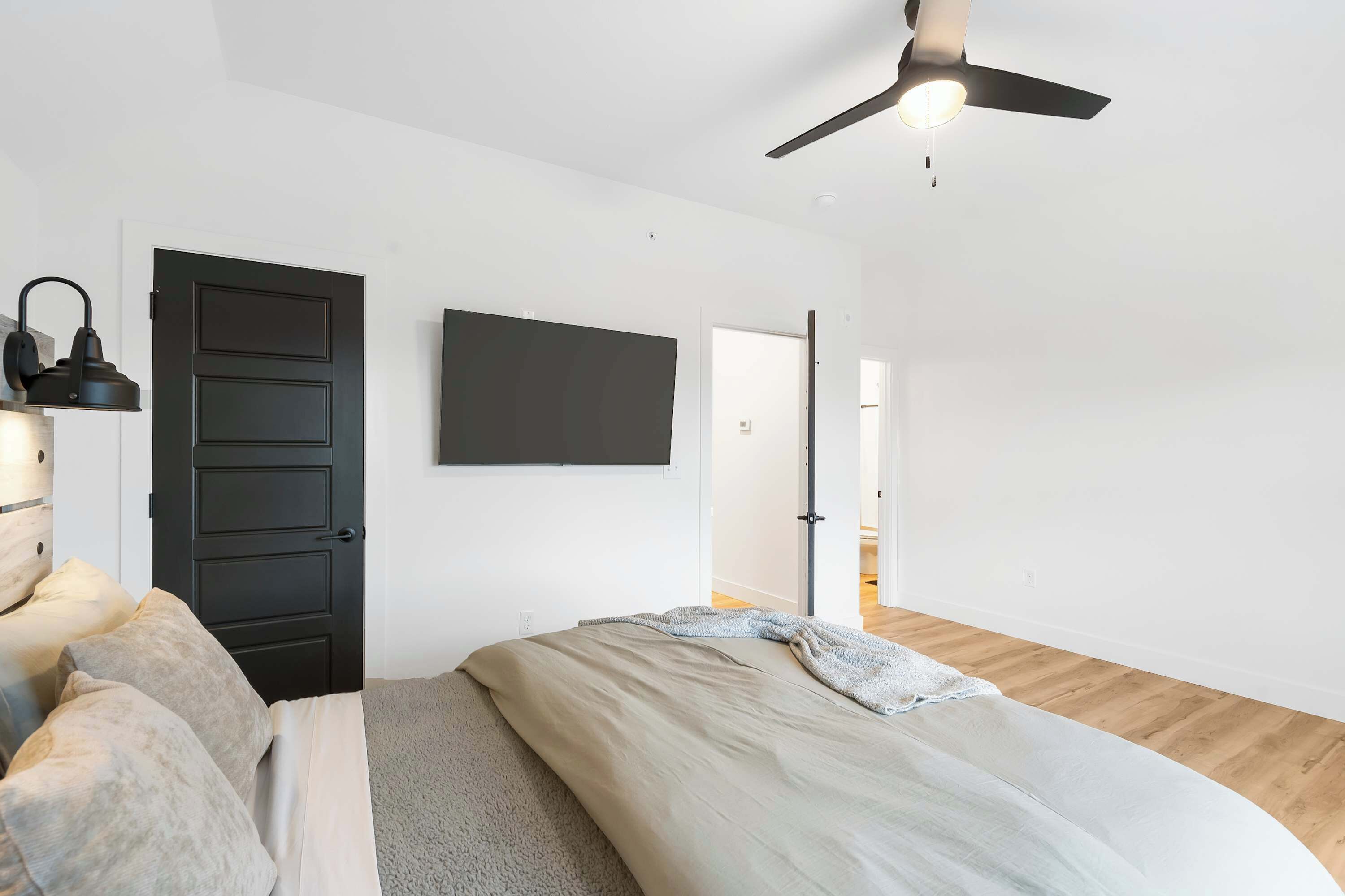 A bedroom with a bed, a ceiling fan, a black door, and a white wall.