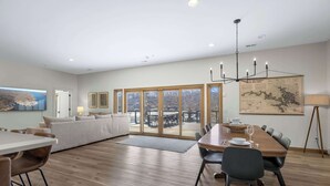 A spacious living area with a dining table, sofa, and large windows offering a view of the outdoors. - Bearcat Bungalows Two Homes One Rental, Sleep 22 (Gravois Mills)