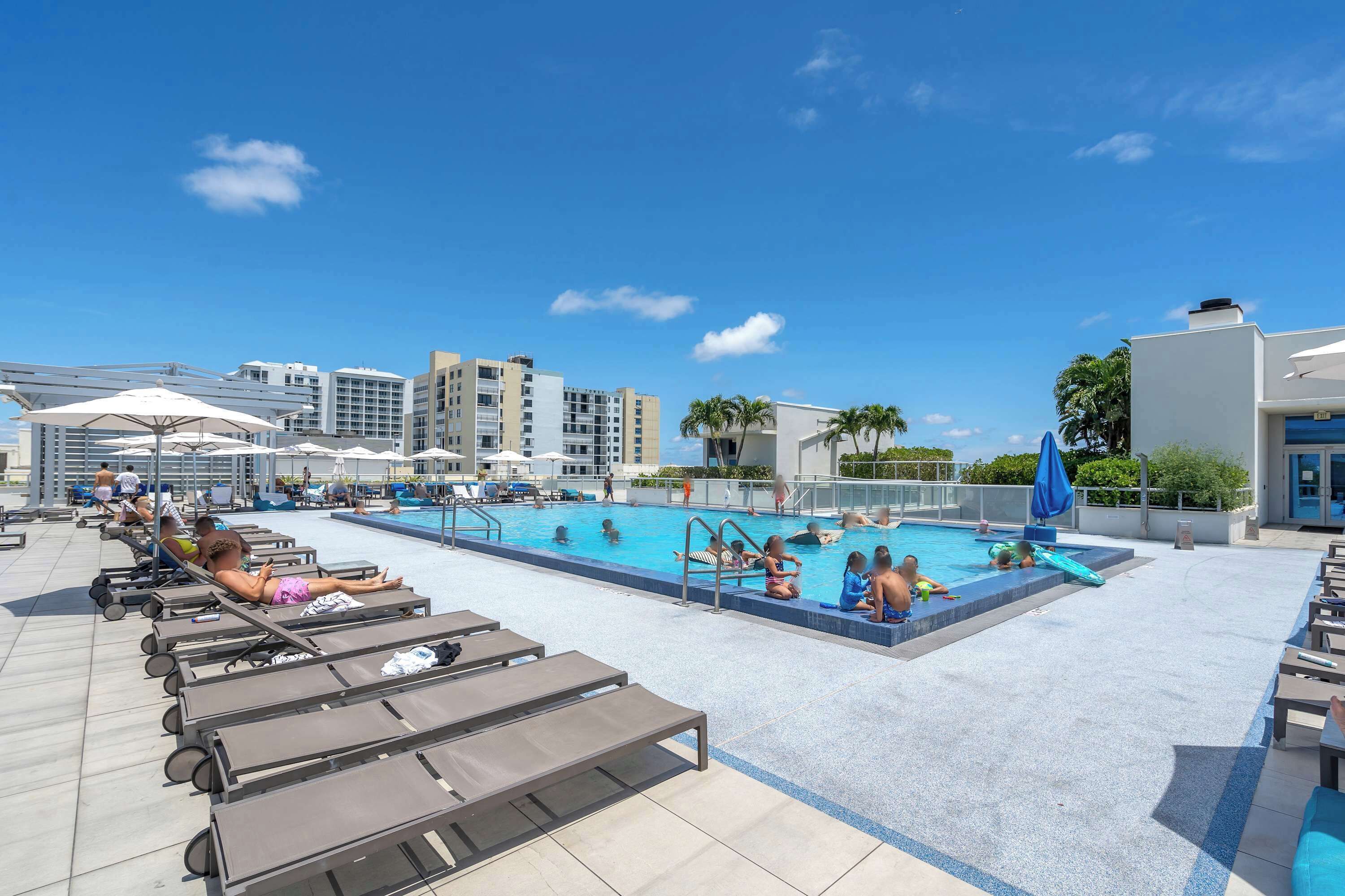 Zona de piscina en la azotea con sillones de descanso, una piscina y edificios modernos al fondo.