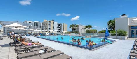 Zona de piscina en la azotea con sillones de descanso, una piscina y edificios modernos al fondo.