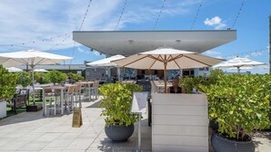 An outdoor seating area with tables and umbrellas, surrounded by potted plants. - Condo Close to the Beach With Rooftop Pool & Gym (Hollywood)