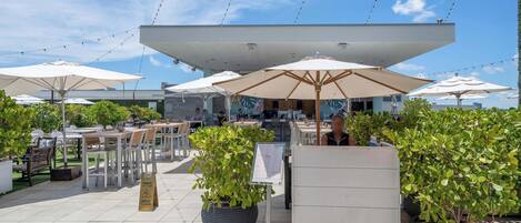 An outdoor seating area with tables and umbrellas, surrounded by potted plants.