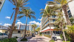 A street lined with palm trees and a building with balconies. - Condo Close to the Beach With Rooftop Pool & Gym (Hollywood)