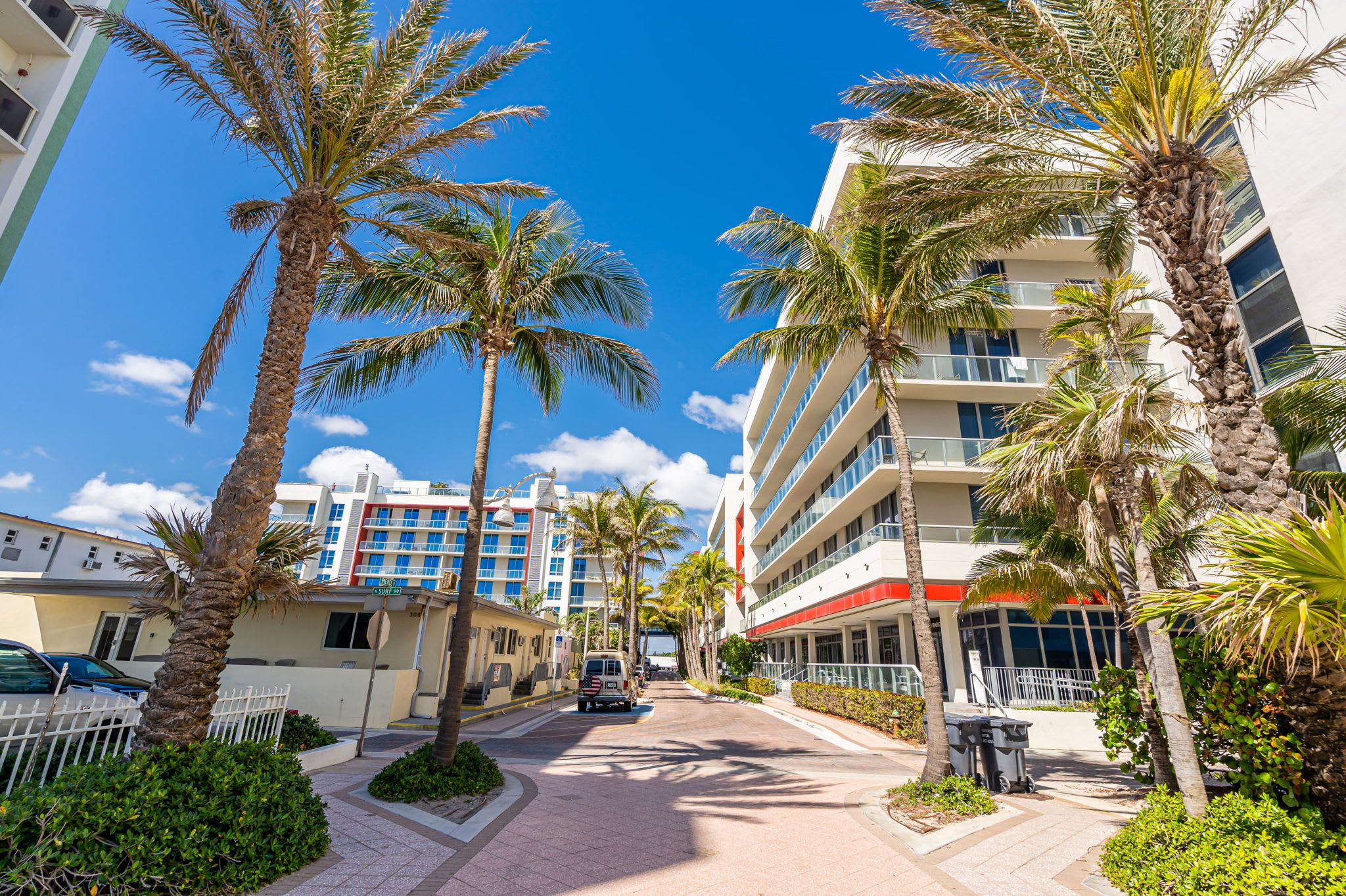 A street lined with palm trees and a multi-story hotel with balconies.