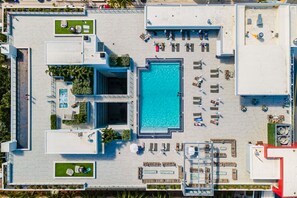 Vista aérea de uma área de piscina no terraço, com vários espaços de estar, uma piscina central e vegetação ao redor.