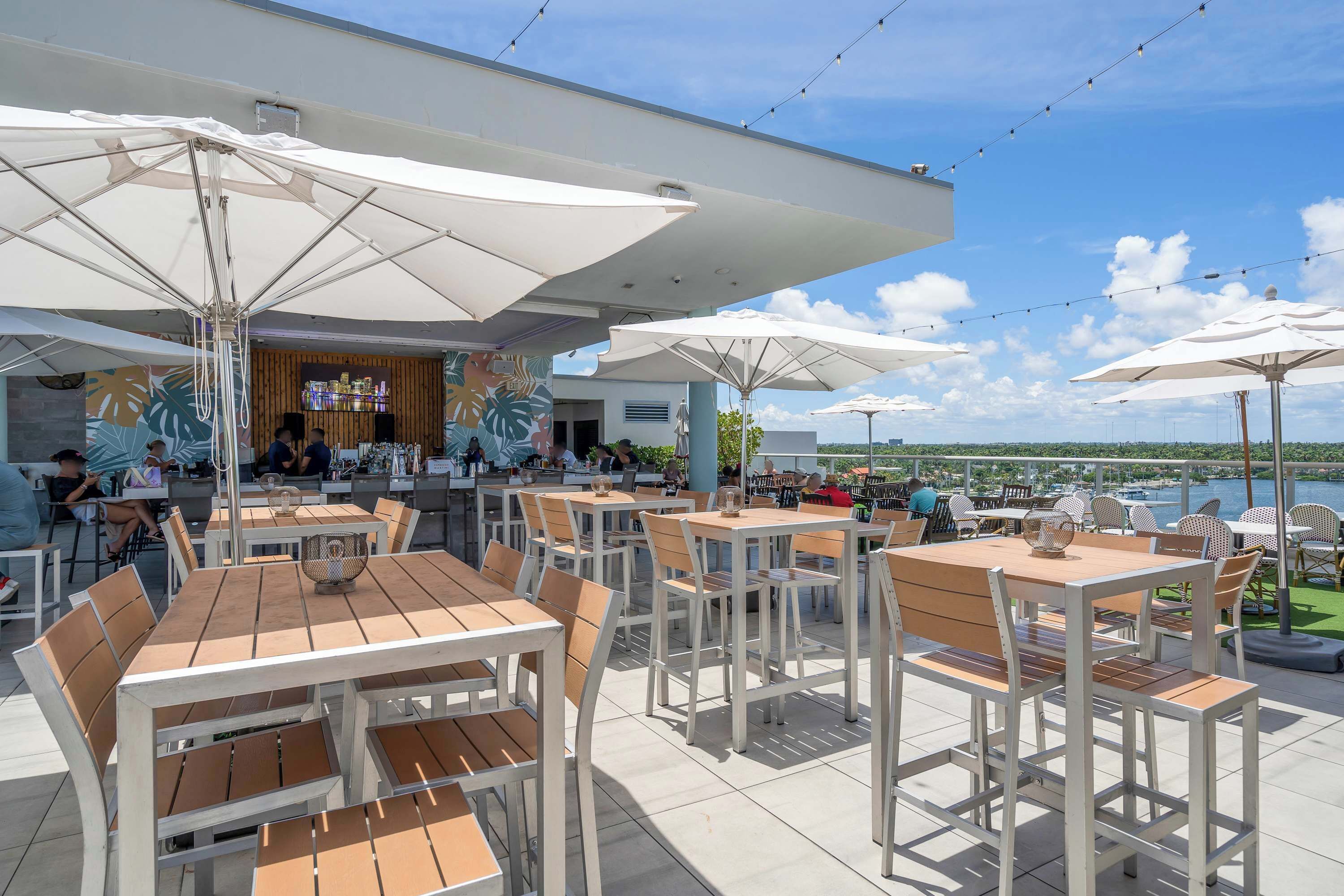 An outdoor dining area with tables and chairs, umbrellas, and a view of the water.
