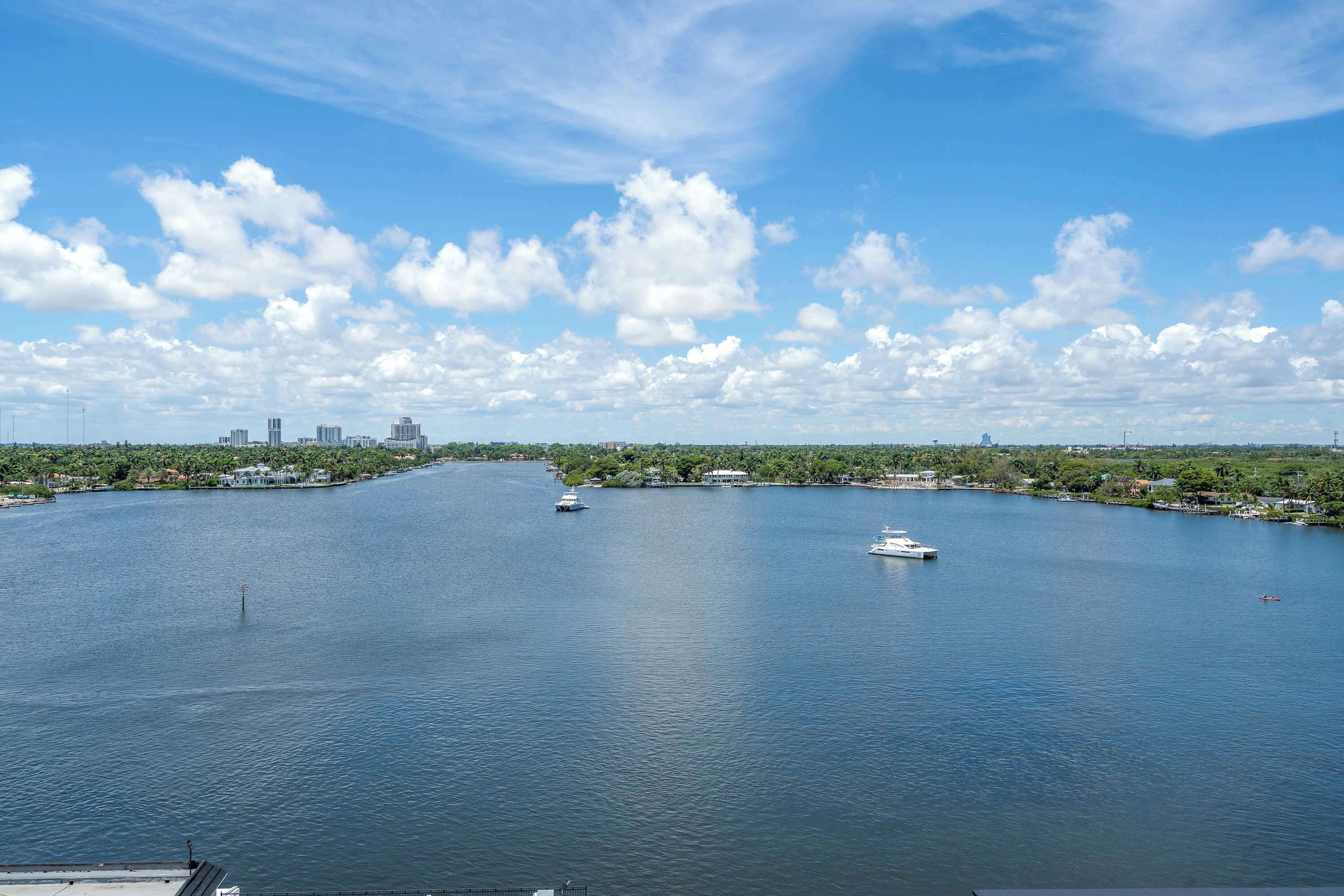 A large body of water with boats, a distant city skyline, and greenery along the shore.