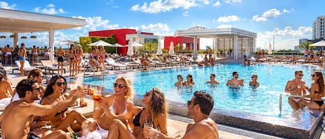 A pool area with lounge chairs, a bar, and a red building in the background.