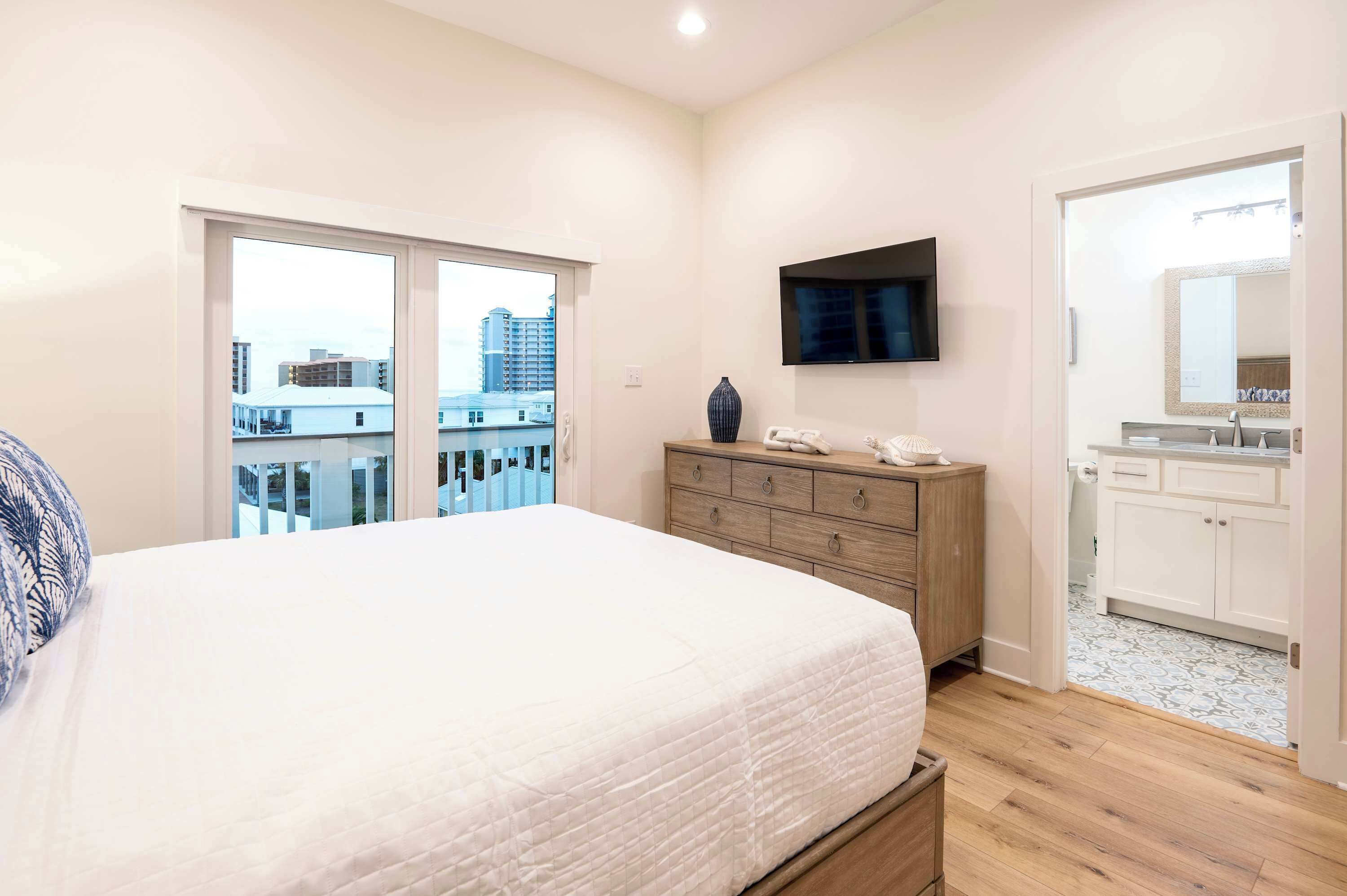 A bedroom with a large bed, a dresser, a TV mounted on the wall, and a bathroom with a mirror and sink.