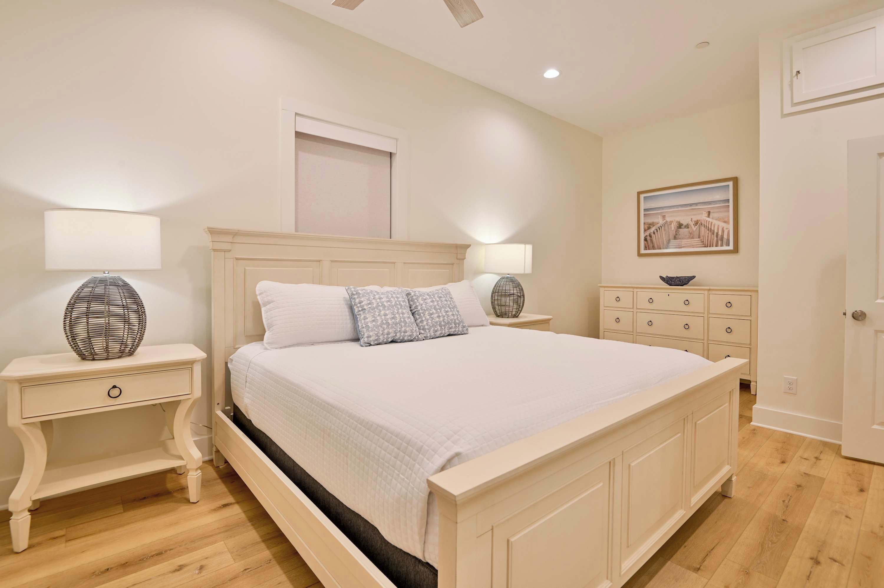 A bedroom with a large bed, two bedside tables with lamps, a dresser, and a framed picture on the wall.