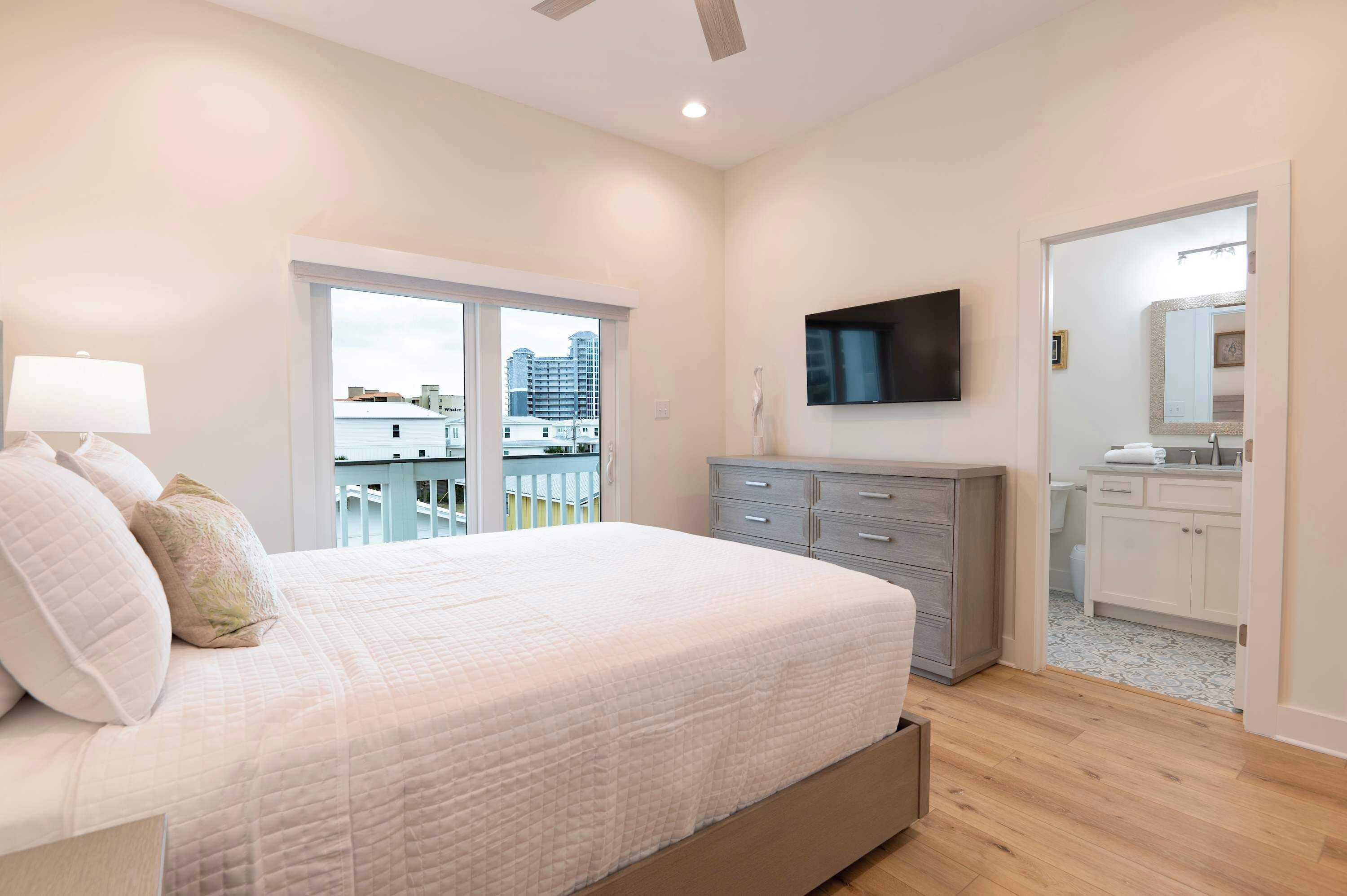 Un dormitorio con cama, televisión, cómoda y baño visible a través de una puerta abierta.