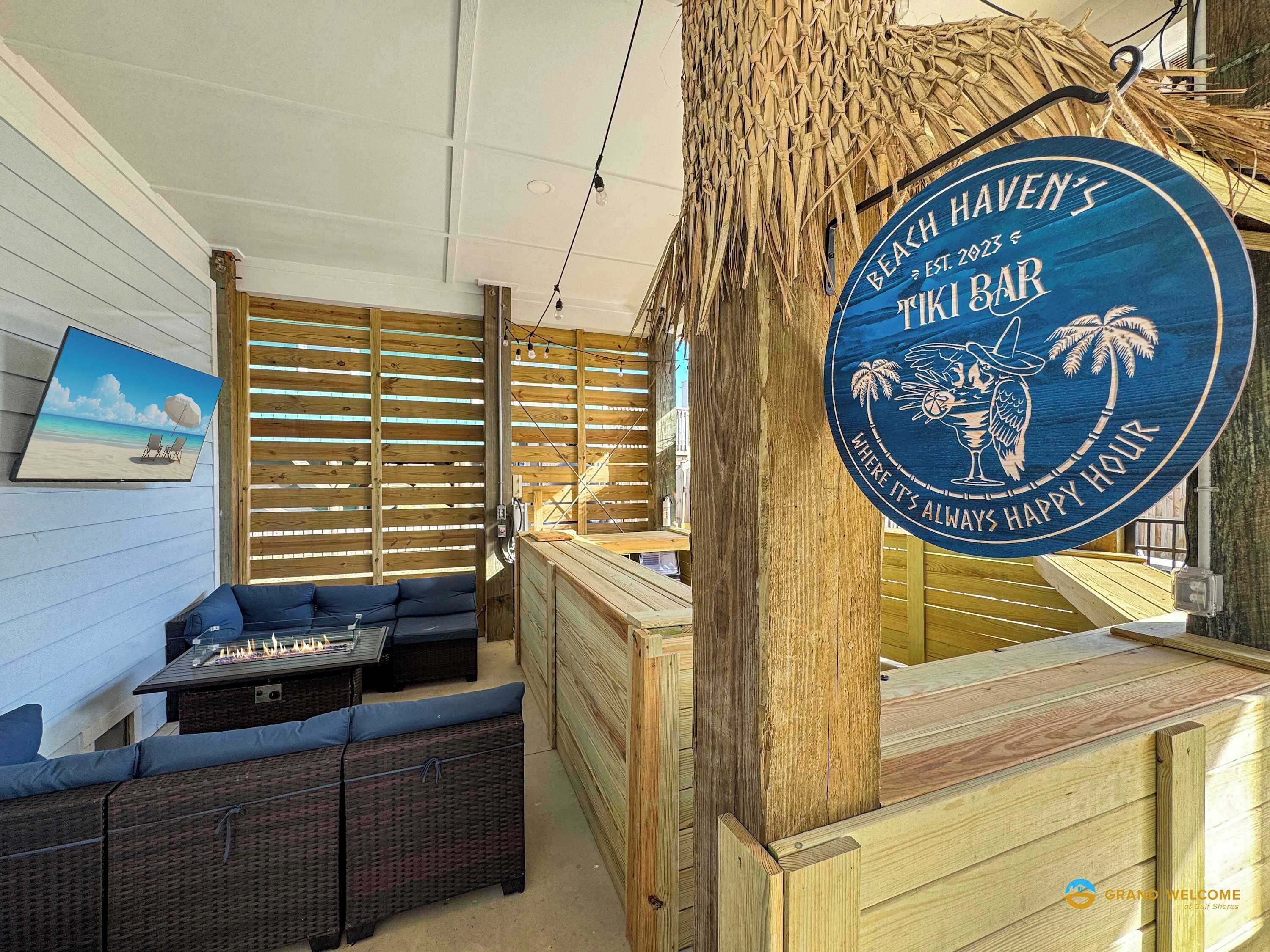 Un bar tiki con interior de madera, un letrero que dice "Beach Haven's Tiki Bar" y vistas de la playa a través de una ventana.