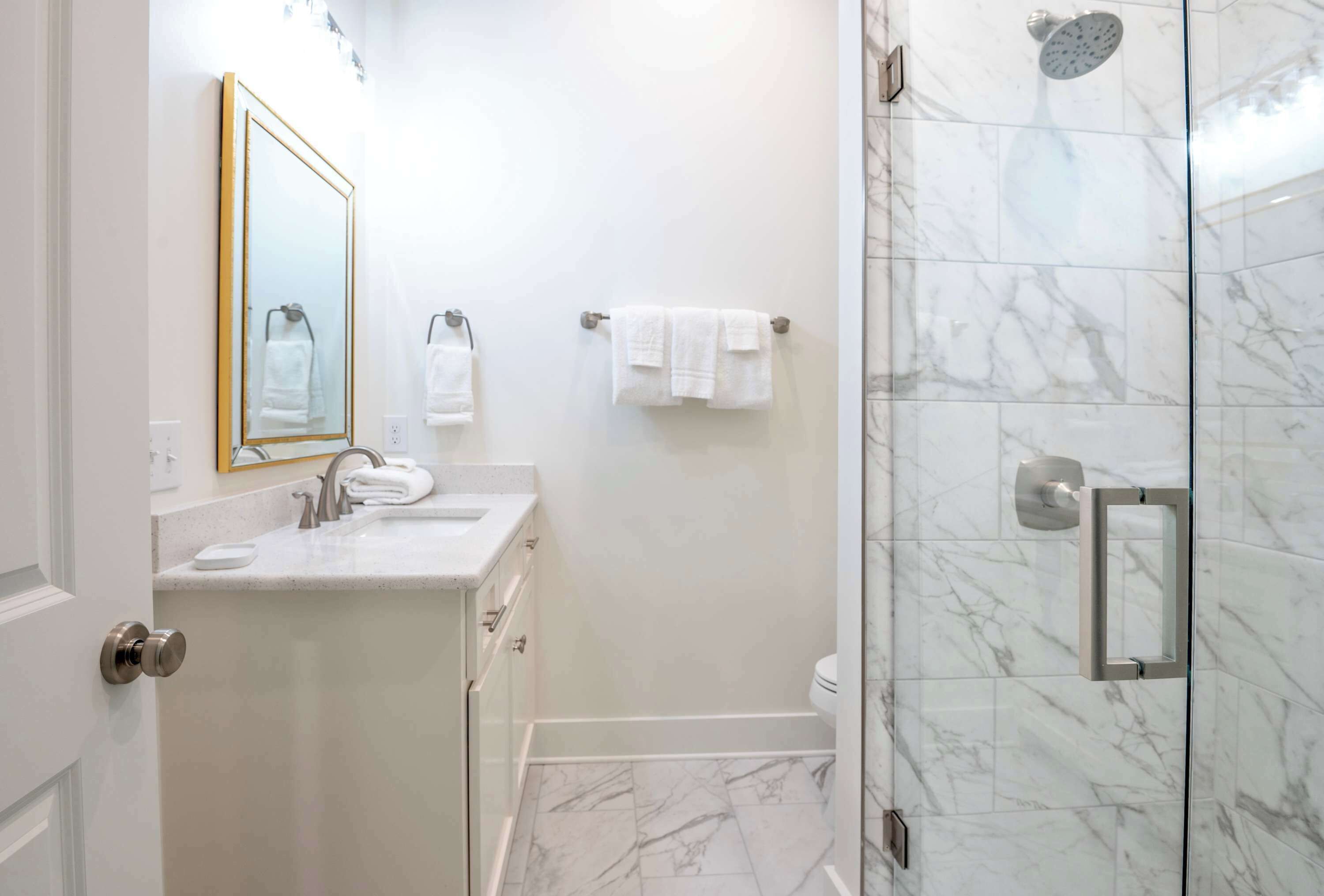 A modern bathroom with a marble floor, a shower with a glass door, and a sink with a mirror.