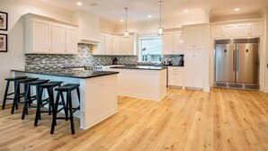 A modern kitchen with white cabinetry, a large island with bar stools, a stainless steel refrigerator, and a patterned backsplash. - 8 Bed 9 Bath Private Pool Grill Walk to Beach (Gulf Shores)