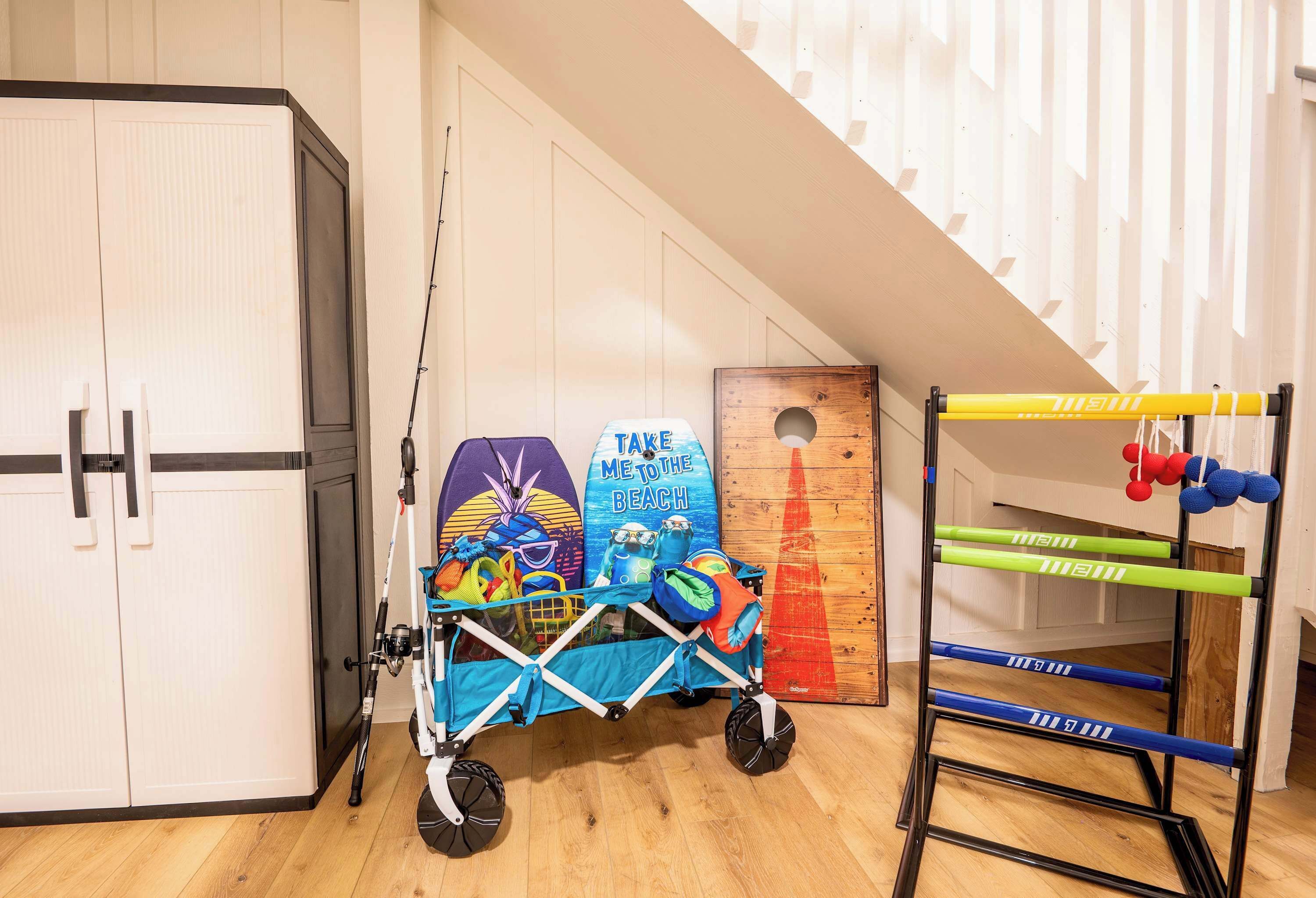 Een kamer met een houten vloer, een witte deur, een blauwe kinderwagen met een strandthema, een klimrek in geel en groen, en een houten wand met een ronde uitsparing.